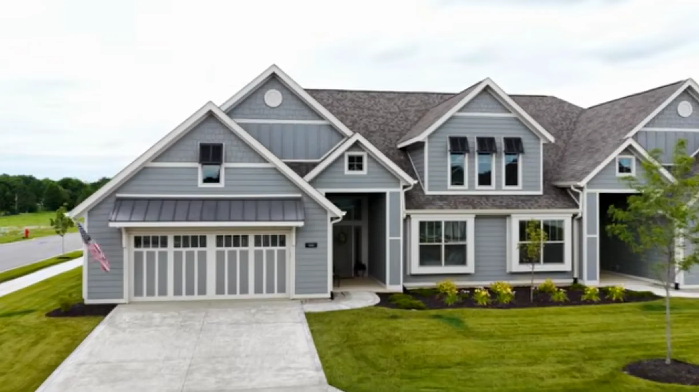 Grayscale suburban home with multiple peaked roofs, white trim, a white garage door, and a manicured front lawn.