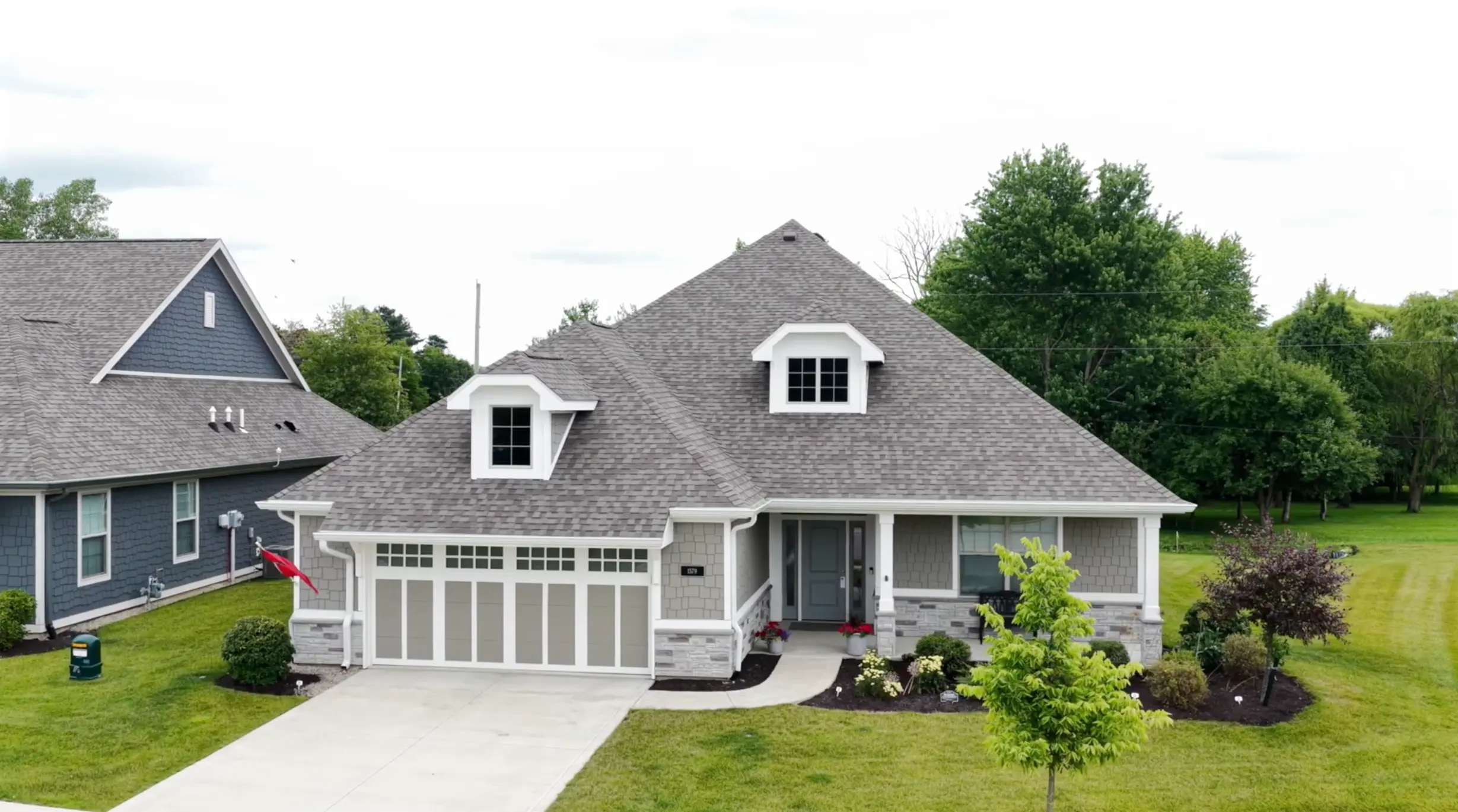Modern gray two-story house with an attached two-car garage, front porch, dormer windows, and a well-kept lawn.